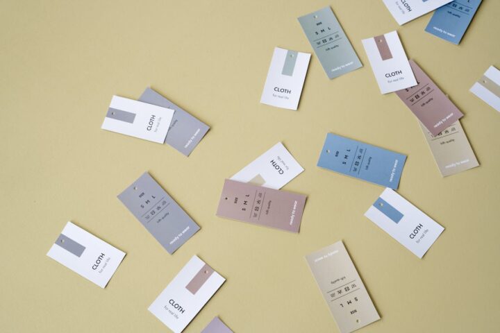 A bunch of clothing tags in white, beige, pink and blue scattered across a beige-ish surface