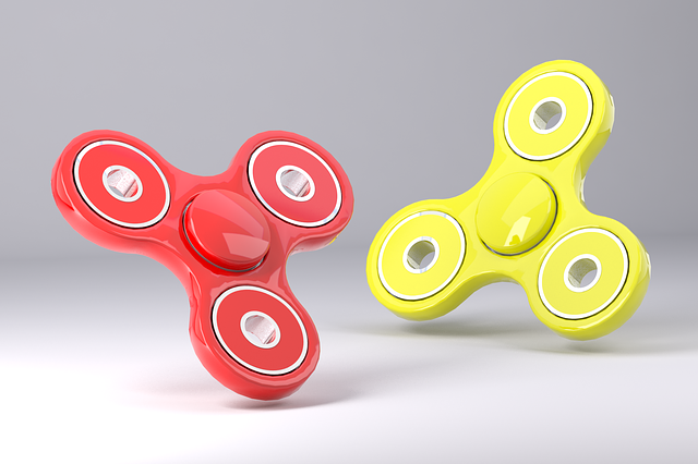 A red and a yellow fidget spinner floating on a white background, at angles similar to a starfish stuck in the sand.